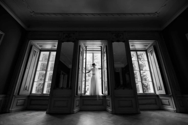 Brud i silhuet foran store vinduer, badet i naturligt lys – et elegant og tidløs bryllupsfotografi.